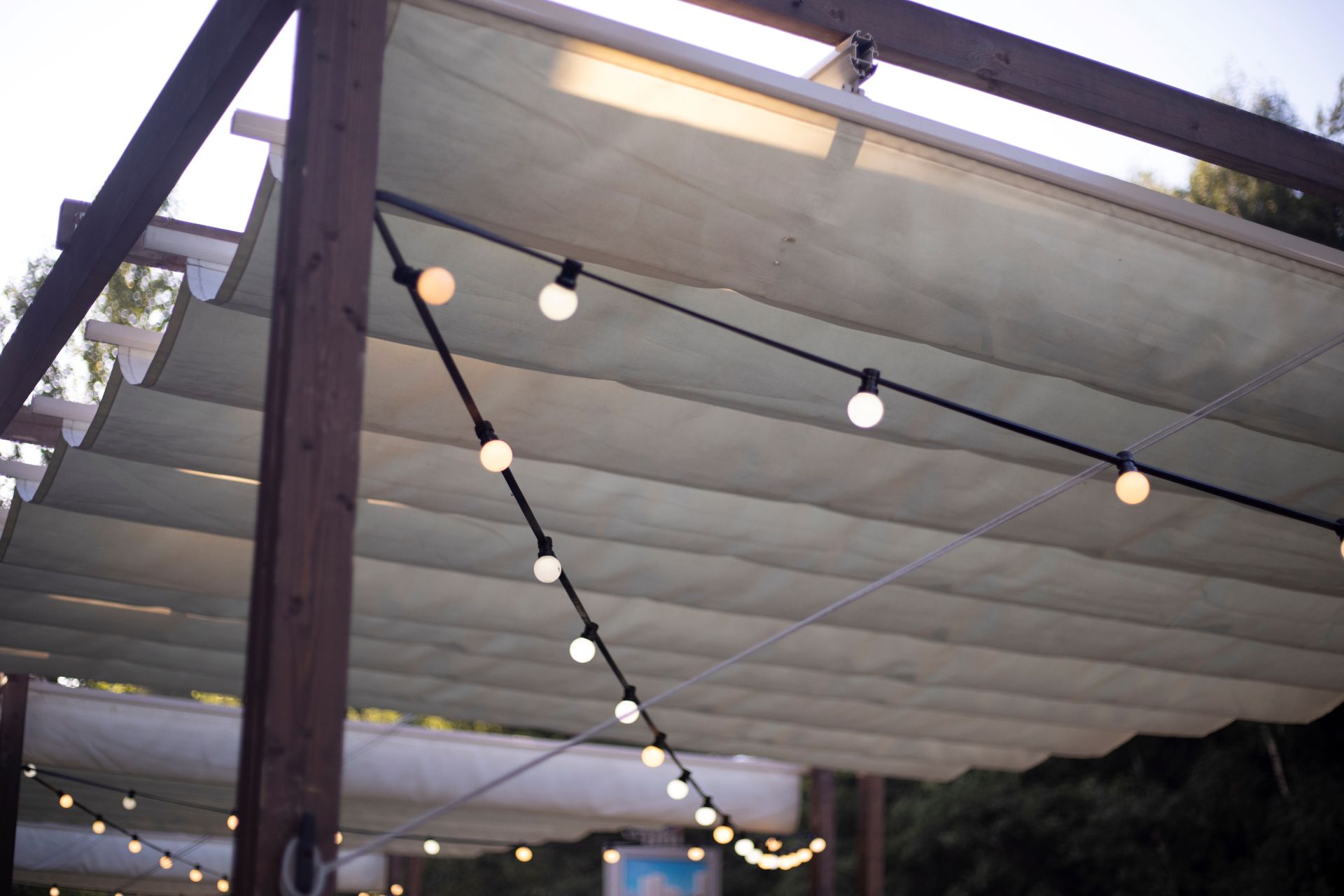 Textiles Stoffsegel mit Lichterkette ueber Terrasse bei Abendlicht, zeigt atmosphaerisches Outdoor-Design mit Sonnensegel nach Mass.