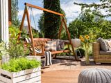 Gemütliche Terrasse mit Holzschaukel, Pflanzen und Lounge-Moebeln im Sommer, perfekt kombiniert mit Sonnensegel nach Mass fuer modernen Outdoor-Luxus.