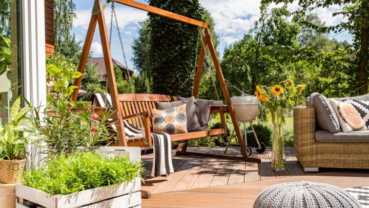 Gemütliche Terrasse mit Holzschaukel, Pflanzen und Lounge-Moebeln im Sommer, perfekt kombiniert mit Sonnensegel nach Mass fuer modernen Outdoor-Luxus.